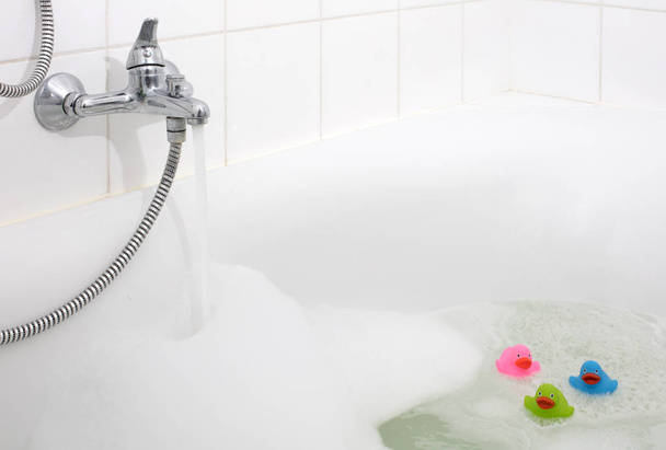 Pink, green and blue duck in a bathtub, surrounded by soap - Valokuva, kuva