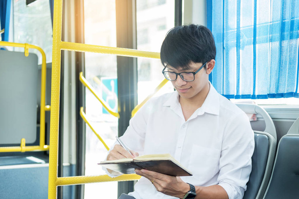 Koncepcja dojazdy, transportu publicznego, mobilności. przystojny młody biznesmen siedzi i czytanie książki na publiczny transport autobusowy. - Zdjęcie, obraz