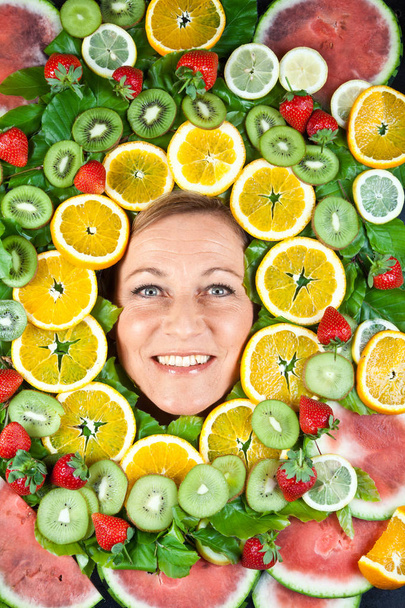 Many fruits stacked together around the head of a cute blond woman - 写真・画像