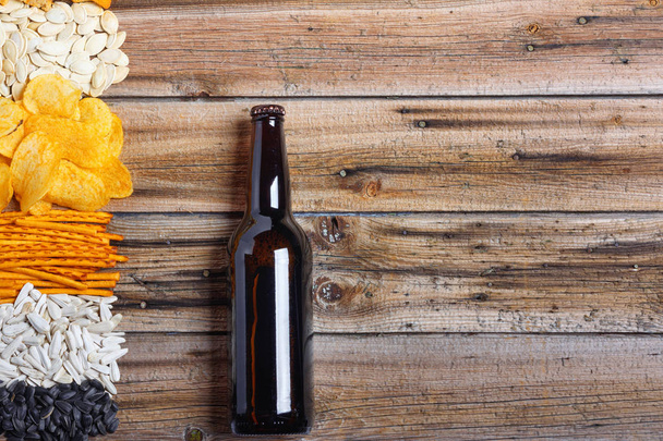 Chips, crackers, seeds, nuts and bottle of fresh cold beer on wooden table. Top view flat lay group objects - Foto, imagen