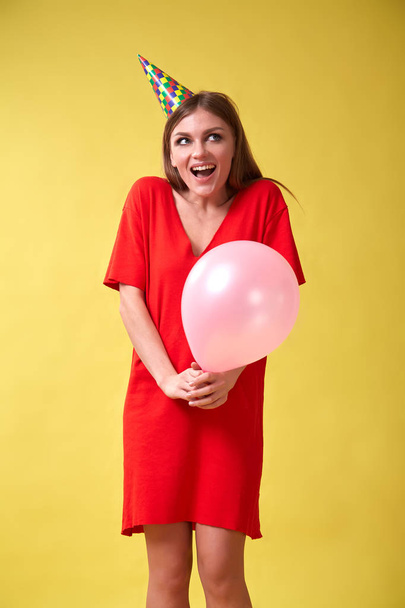 Girl in red dress and birthday hat holding a christmas balloon in her hands. - Фото, изображение