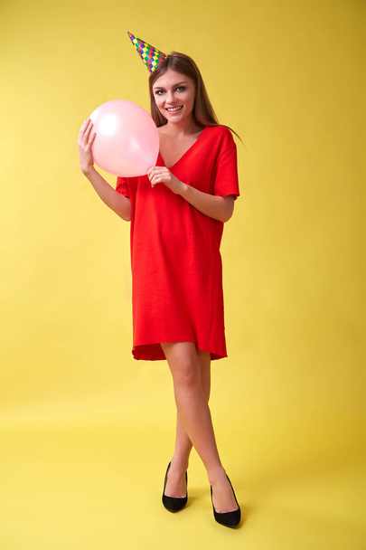 Girl in red dress and birthday hat holding a christmas balloon in her hands. - Foto, imagen