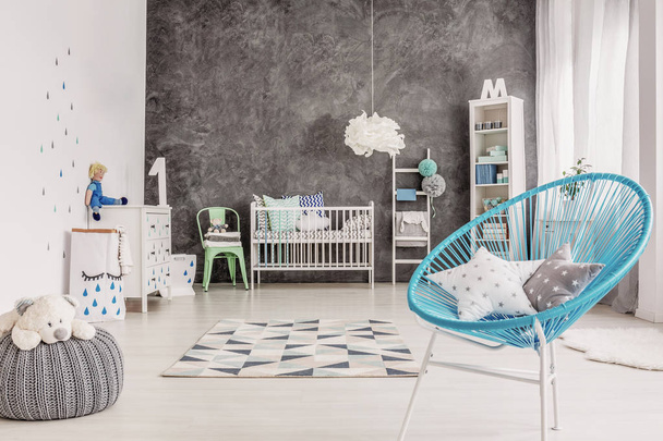 Star pillows on blue armchair in grey baby's bedroom interior with teddy bear on pouf. Real photo - Foto, imagen