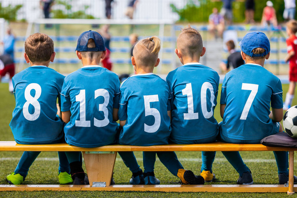 試合中に子供のサッカー チーム。少年サッカー チームのメンバーに草のフィールド サッカーのベンチに座っています。ピッチ スタジアムでボールと子供たちのフットボール チーム。子供のスポーツのサッカーのチーム - 写真・画像