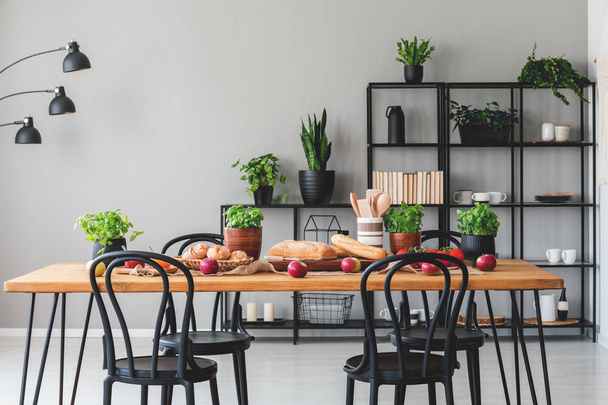 Wooden table with healthy food in grey dining room interior with black chairs and plants. Real photo - Fotó, kép