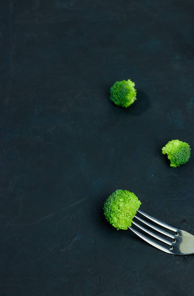 Fresh green broccoli cabbage lies on a fork. Template of healthy food on a dark background. Copy space Top view. Vegetarian food. view from above. - Fotó, kép