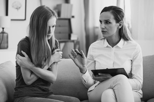 Black and white photo of professional pedagogue relieving stress of young teenage girl during psychotherapy. Mental health concept. - Фото, изображение