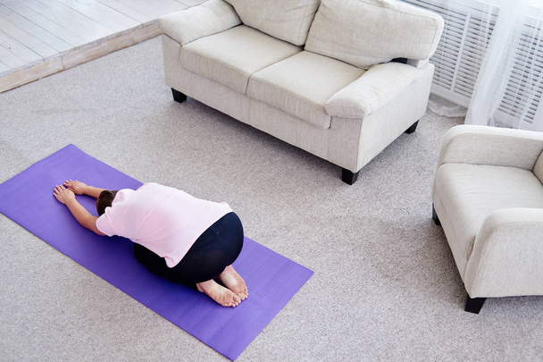 Portrait of young woman practicing yoga at home indoor, copy space. Girl relax meditation in child's pose, full length. Relaxing and doing yoga, resting, stretching. Wellness and healthy lifestyle. Balasana - Photo, Image