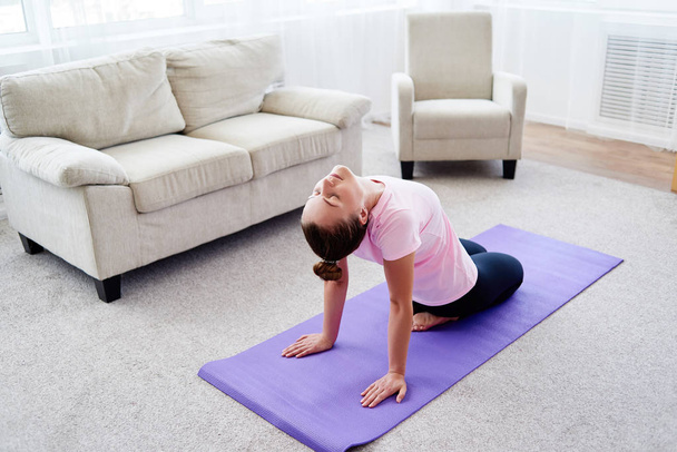 Portrait of young woman practicing yoga at home indoor, copy space. Girl stretching on mat, full length. Relaxing and doing yoga. Wellness and healthy lifestyle - Fotografie, Obrázek