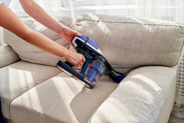 Close up of woman hand with vacuum cleaner, copy space. Woman cleaning sofa with vacuum cleaner. Household and spring-cleanig concept - Foto, afbeelding