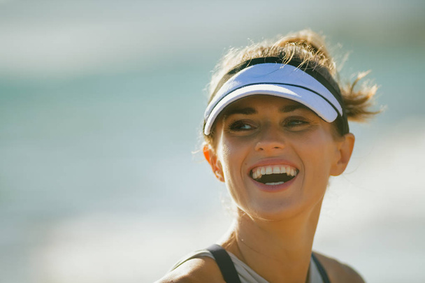 Portrait of smiling fit sports woman in fitness clothes on the seacoast in the evening.  beautiful summer day. 30 something years old woman take advantage of fresh air outside workout - Foto, Imagem