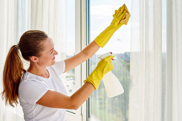 Donna in camicia bianca e guanti di gomma gialla pulizia finestra con spray detergente e straccio giallo a casa o in ufficio, spazio copia, vista posteriore. Persone, lavori domestici e concetto di pulizia
 - Foto, immagini