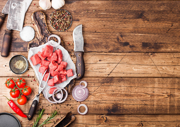 Raw lean diced casserole beef pork steak with vintage meat hatchet and knife on wooden background. Salt and pepper with fresh rosemary, red onion and garlic. - Фото, зображення