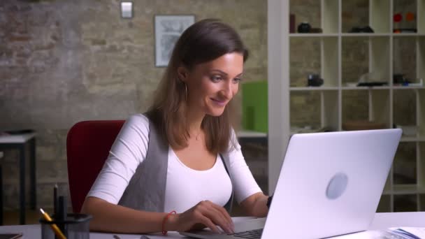 Attractive female office worker sitting in front of the laptop and getting extremely happy when finds out the good news on the workplace - Imágenes, Vídeo
