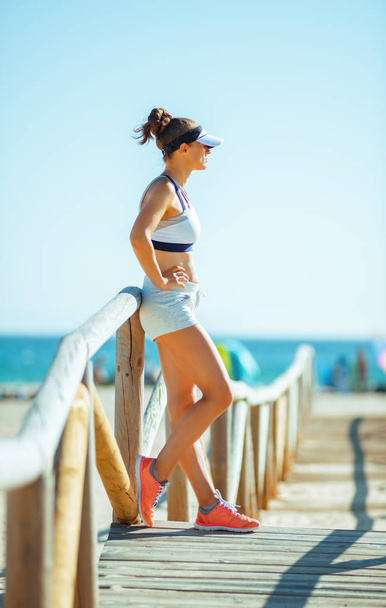 young woman jogger in sport clothes on the seashore looking into the distance. exercise improves not only your health but also your mood. workout on the seashore even more calming and stress relieving - Fotoğraf, Görsel