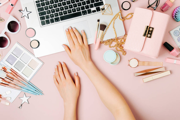 Fashion blogger working with laptop. Workspace with  female accessory, cosmetics products on pale pink table. flat lay, top view - Foto, immagini