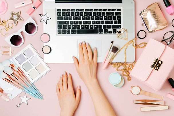 Fashion blogger working with laptop. Workspace with  female accessory, cosmetics products on pale pink table. flat lay, top view - Foto, Bild