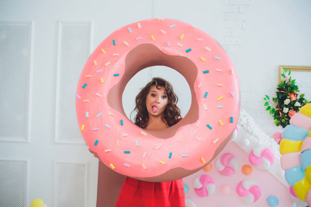 cute girl posing with pink donuts, fooling around, dessert, bad food, looks into the hole in the donut, keeps donuts by the eyes - Фото, изображение