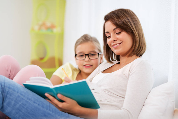 happy girl with mother reading book at home - Φωτογραφία, εικόνα