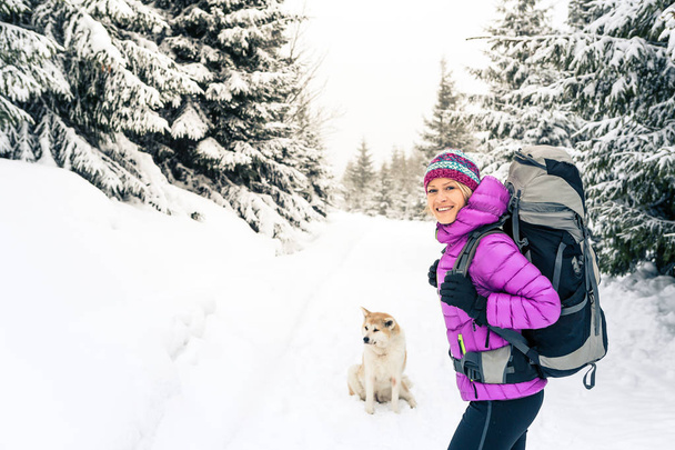 Happy girl hiking in white winter forest with akita dog. Recreation fitness and healthy lifestyle outdoors in nature. Inspirational winter landscape. - Photo, Image