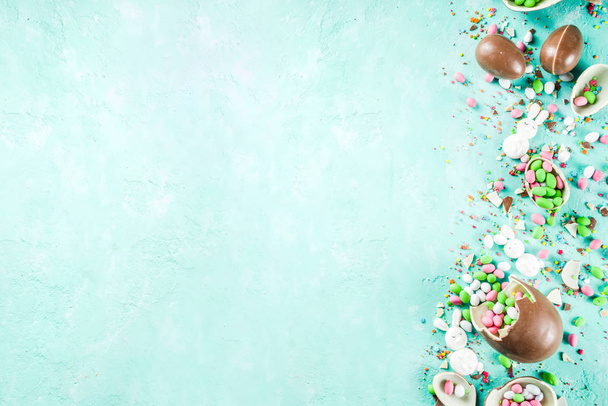Colorful spring easter sweets background, with chocolate eggs, sugar sprinkles and marshmallow bunny, turquoise light blue concrete background copy space top view - Fotografie, Obrázek