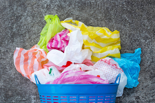 Красочные пластиковые пакеты с корзиной для мусора на фоне цементного пола
.  - Фото, изображение