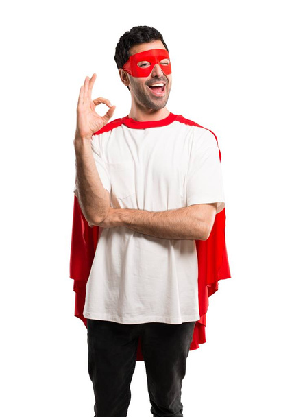 Szuperhős ember a maszk és a piros köpeny mutatja az ok jele, ujjaival, miközben szemmel Kacsintó elszigetelt fehér background - Fotó, kép
