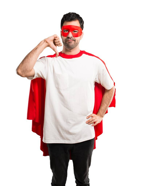スーパー ヒーロー マスクと赤マントは親指で下を負の式と記号を示す男。孤立した白い背景の悲しそうな表情 - 写真・画像