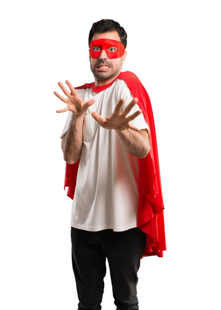 El hombre superhéroe con máscara y capa roja está un poco nervioso y asustado estirando las manos al frente sobre un fondo blanco aislado
 - Foto, imagen