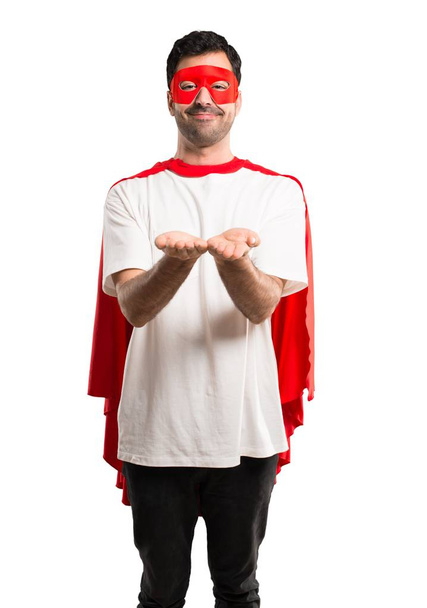 Superhelden-Mann mit Maske und rotem Umhang hält imaginären Kopierraum auf die Handfläche, um eine Anzeige auf isoliertem weißem Hintergrund einzufügen - Foto, Bild