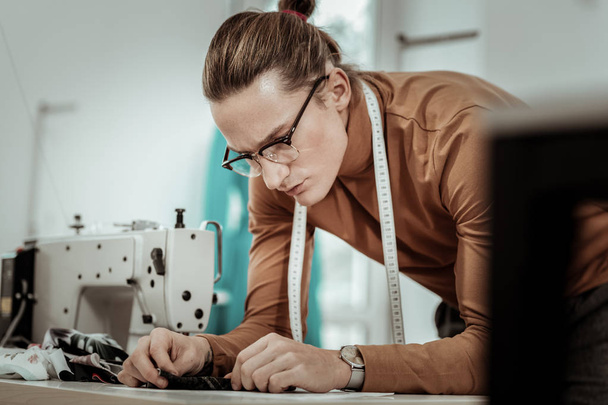 Young fashion dressmaker in eyeglasses tailoring a new dress - Foto, Bild