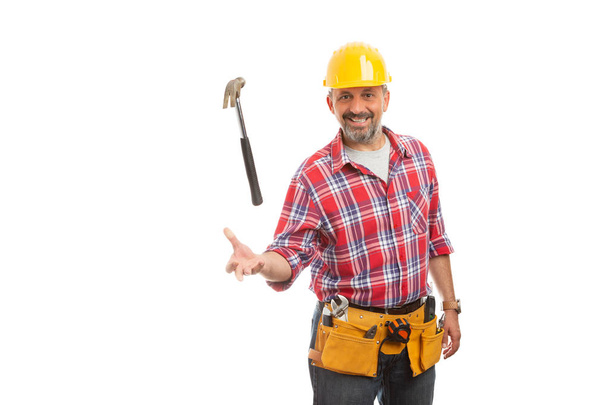 Sonriente constructor masculino lanzando martillo en el aire como truco con expresión amistosa aislada en blanco
 - Foto, Imagen