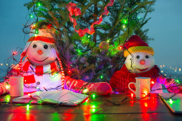Χριστούγεννα οικογενειακά έννοια. Δύο χιονάνθρωπους για καπέλα και φουλάρια με καρότο μύτη και αστεία χαμόγελα. Φλιτζάνι ζεστά ποτά στο τραπέζι, Χριστούγεννα και ζεστό. Ευτυχισμένος ο καινούριος χρόνος - Φωτογραφία, εικόνα