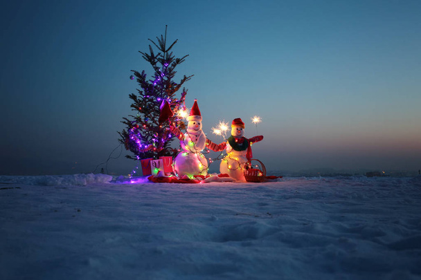 Perheloma. Onnelliset lumiukot pitelevät bengalivaloja. Kirkkaat valot yöllä lunta. Seppeleitä ja palavia valoja lumiukon ympärillä. Säihkyvät
 - Valokuva, kuva