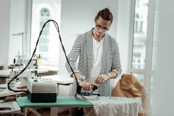 Stylish young fashion designer in a striped jacket doing ironing - Фото, зображення
