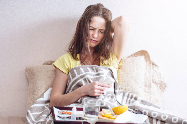 A girl with a headache and flu in bed is treated with tablets and vitamins. Seasonal colds in winter - Photo, Image