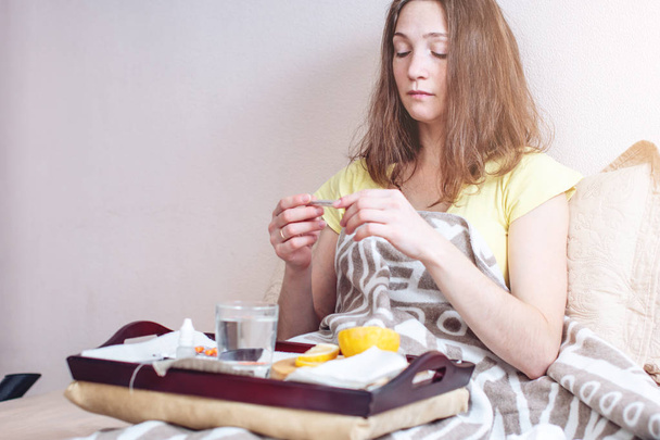 A girl with a headache and flu in bed is treated with tablets and vitamins. Seasonal colds in winter - Foto, imagen