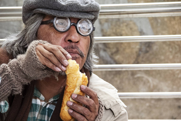 Άστεγος άνθρωπος πορτρέτο τρώει παλιό ψωμί στο δρόμο walkway στην πρωτεύουσα. - Φωτογραφία, εικόνα