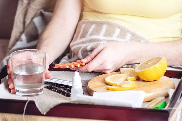 Thermometer pills water and lemon on tray. A person with a cold is treated in bed. Colds, flu and treatment - Foto, Imagem