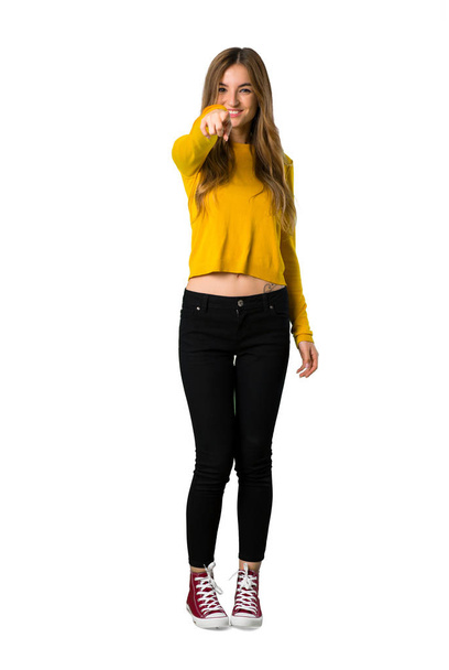 Un plan complet d'une jeune fille avec un pull jaune pointe du doigt vers vous avec une expression confiante sur fond blanc isolé
 - Photo, image