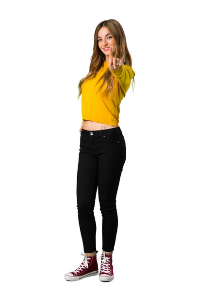Um tiro de comprimento total de uma jovem com suéter amarelo mostrando e levantando um dedo no fundo branco isolado
 - Foto, Imagem