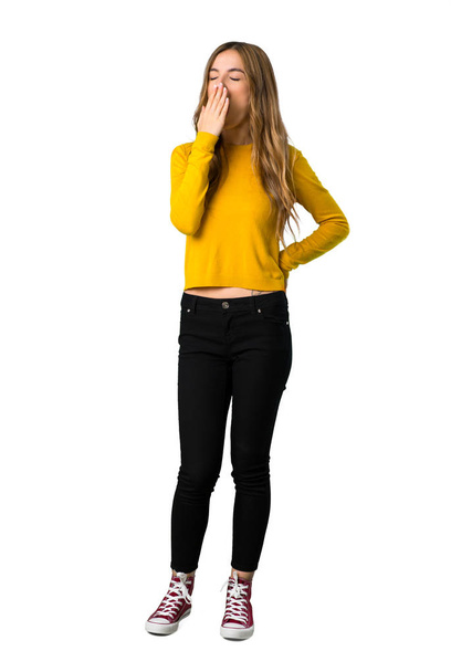 Um tiro de comprimento total de uma jovem com suéter amarelo bocejando e cobrindo a boca aberta com a mão sobre fundo branco isolado
 - Foto, Imagem