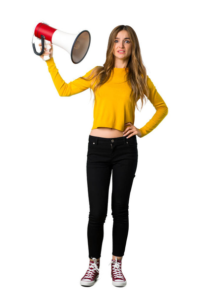 A full-length shot of a young girl with yellow sweater taking a megaphone that makes a lot of noise on isolated white background - Foto, Imagem