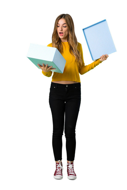 A full-length shot of a young girl with yellow sweater holding gift box in hands on isolated white background - Photo, image