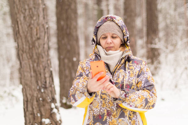 Une femme compose un numéro de téléphone. Parler avec l'utilisation de la communication cellulaire. Forêt d'hiver à la périphérie de la ville
. - Photo, image
