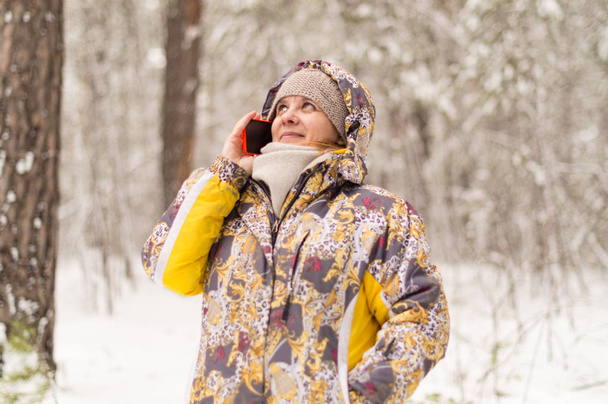Une femme compose un numéro de téléphone. Parler avec l'utilisation de la communication cellulaire. Forêt d'hiver à la périphérie de la ville
. - Photo, image