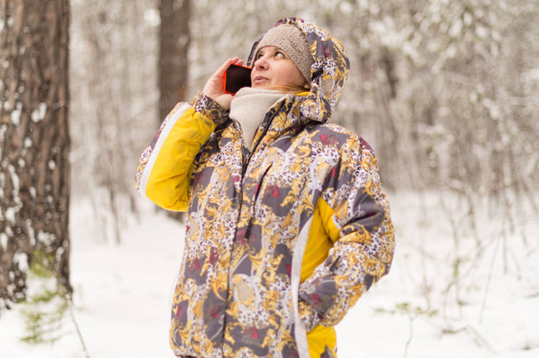 Egy asszony, telefonszám tárcsázása. Beszél a sejtes kommunikáció használata. Téli erdő a város szélén. - Fotó, kép