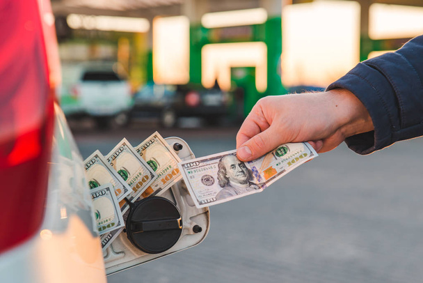 Мужская рука кладет деньги в автомобильный бак. заправка машины. концепция автозаправочной станции
 - Фото, изображение