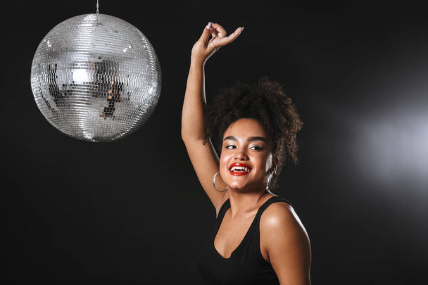 Beautiful african woman standing with silver disco ball isolated over black background, dancing - Valokuva, kuva