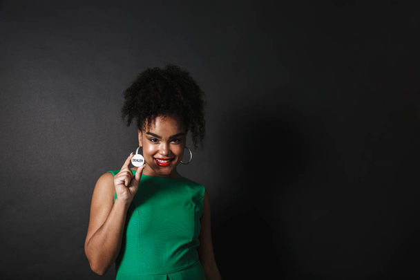 Photo of pretty afro american woman wearing green dress showing casino token isolated over dark background - Foto, imagen